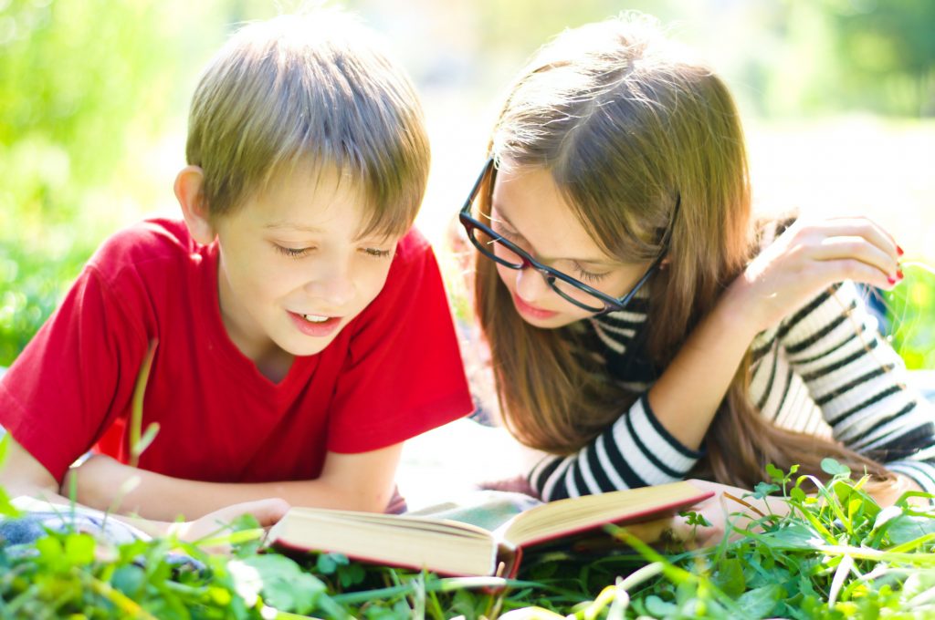 Two children reading a book on grass
